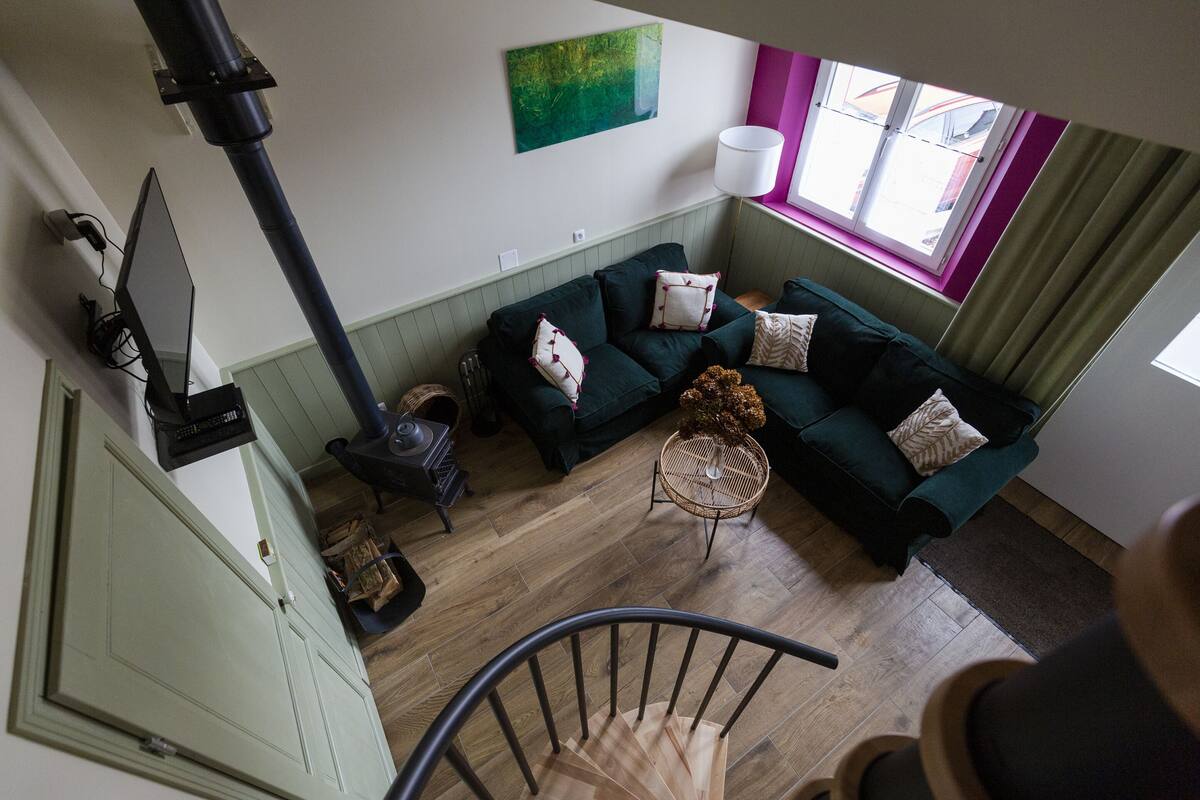 Una sala de estar con un sofá verde, una chimenea, una ventana con cortinas y una escalera.