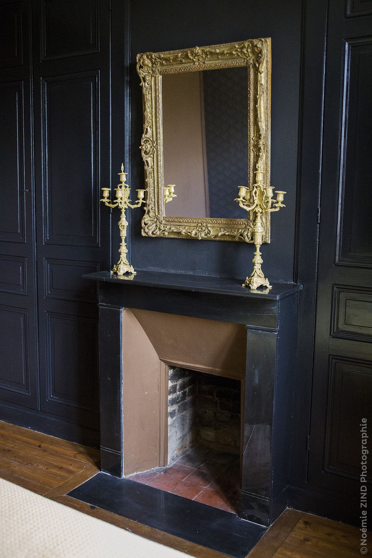 A black fireplace with a gold-framed mirror above it.
