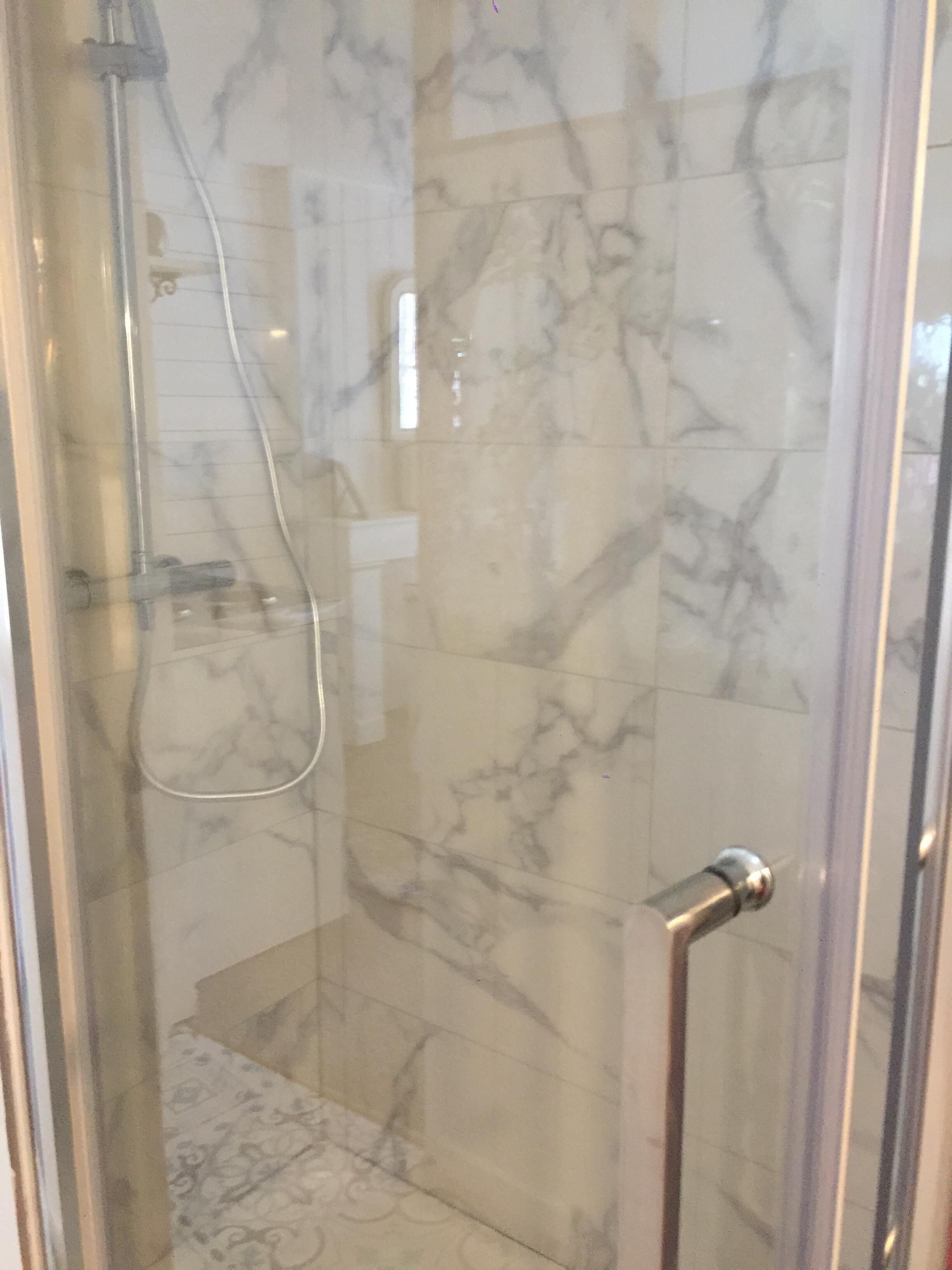 A glass-enclosed shower area with marble tiles and a handheld showerhead.