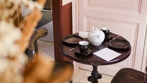 Een gedekte tafel met een theepot, kopjes en schotels, met een stoel en een deur op de achtergrond.