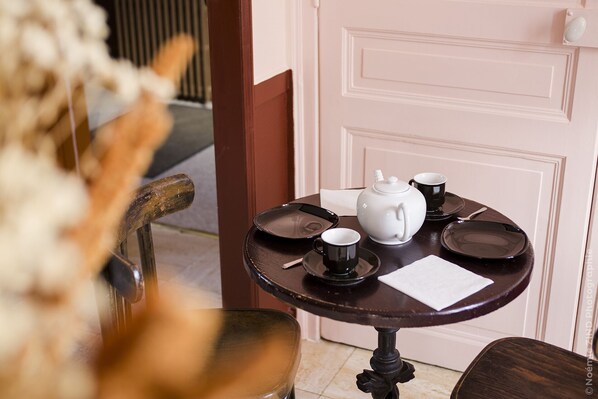 Une table dressée avec une théière, des tasses et des soucoupes, une chaise et une porte en arrière-plan.
