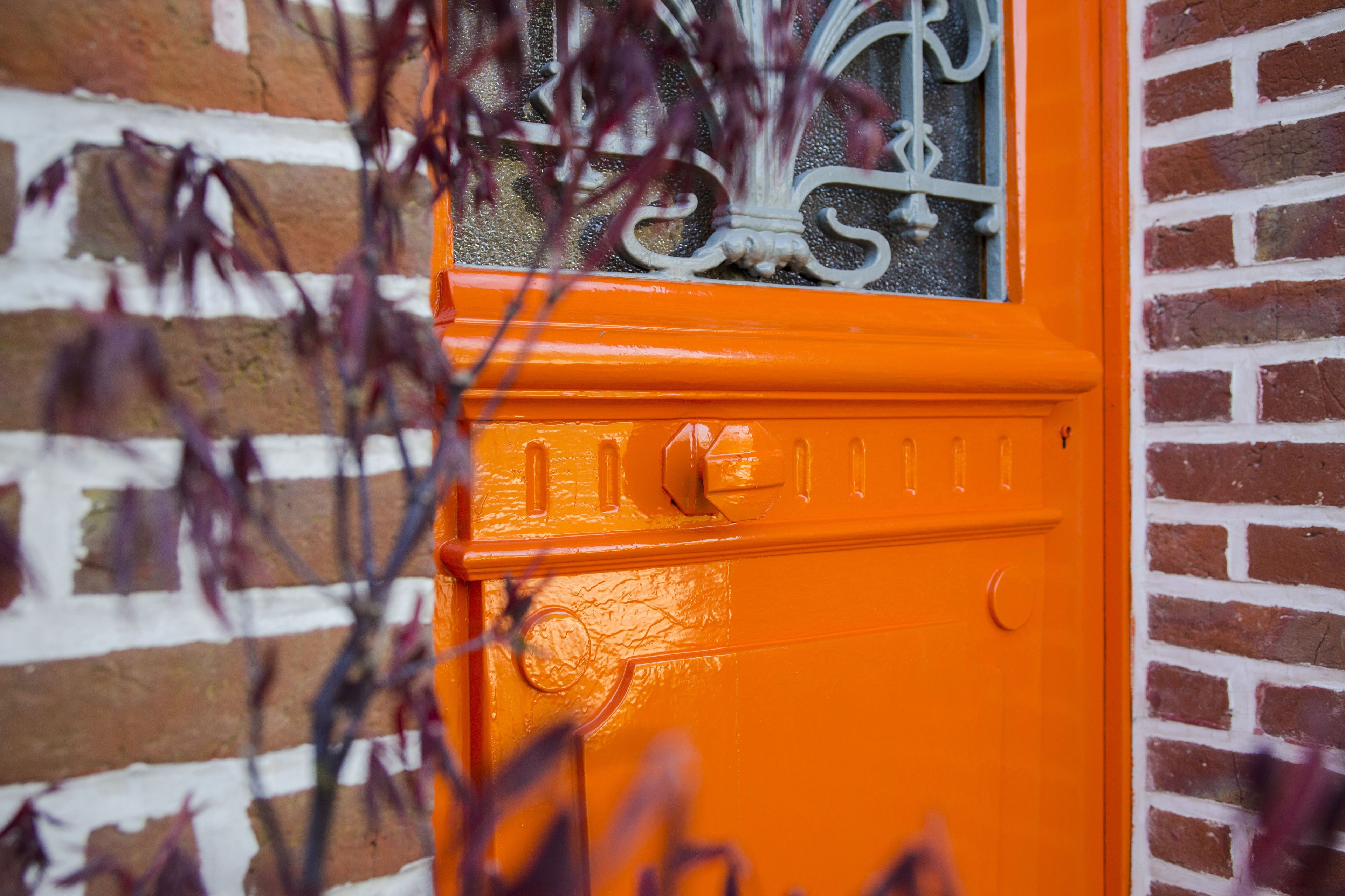 A bright orange door with a decorative window and a metal handle.