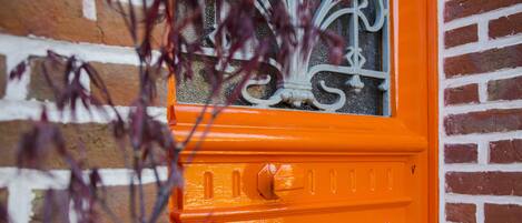 Eine leuchtend orangefarbene Tür mit einem Zierfenster und einer Metallbeschlag.
