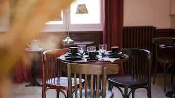 Ein Essbereich mit einem runden Tisch, gedeckt für vier Personen, umgeben von Holzsesseln. Im Hintergrund ist eine Lampe und ein kleiner Tisch mit einem Teekessel zu sehen.
