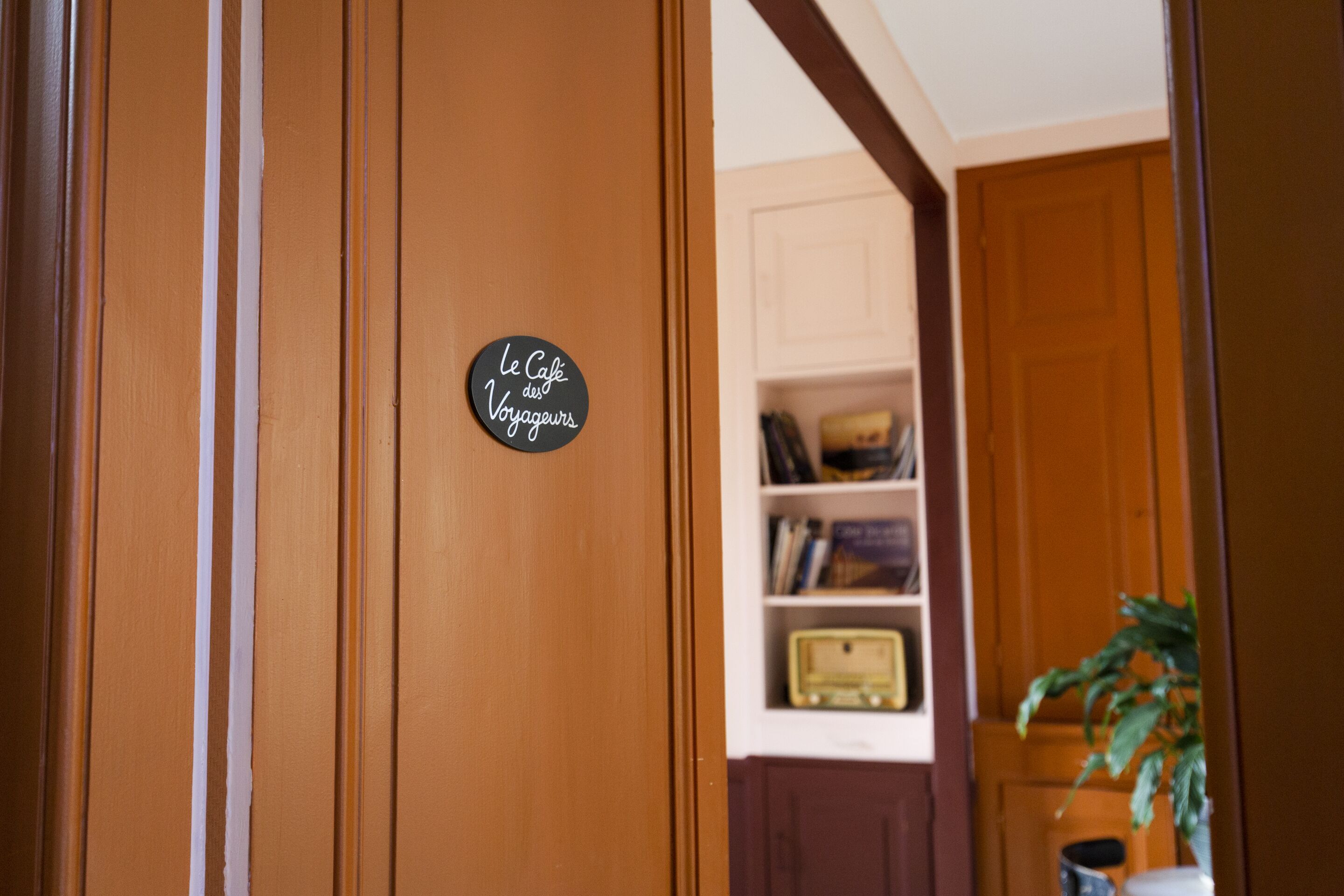 A wooden door with a sign that reads 'Le Café des Voyageurs.'