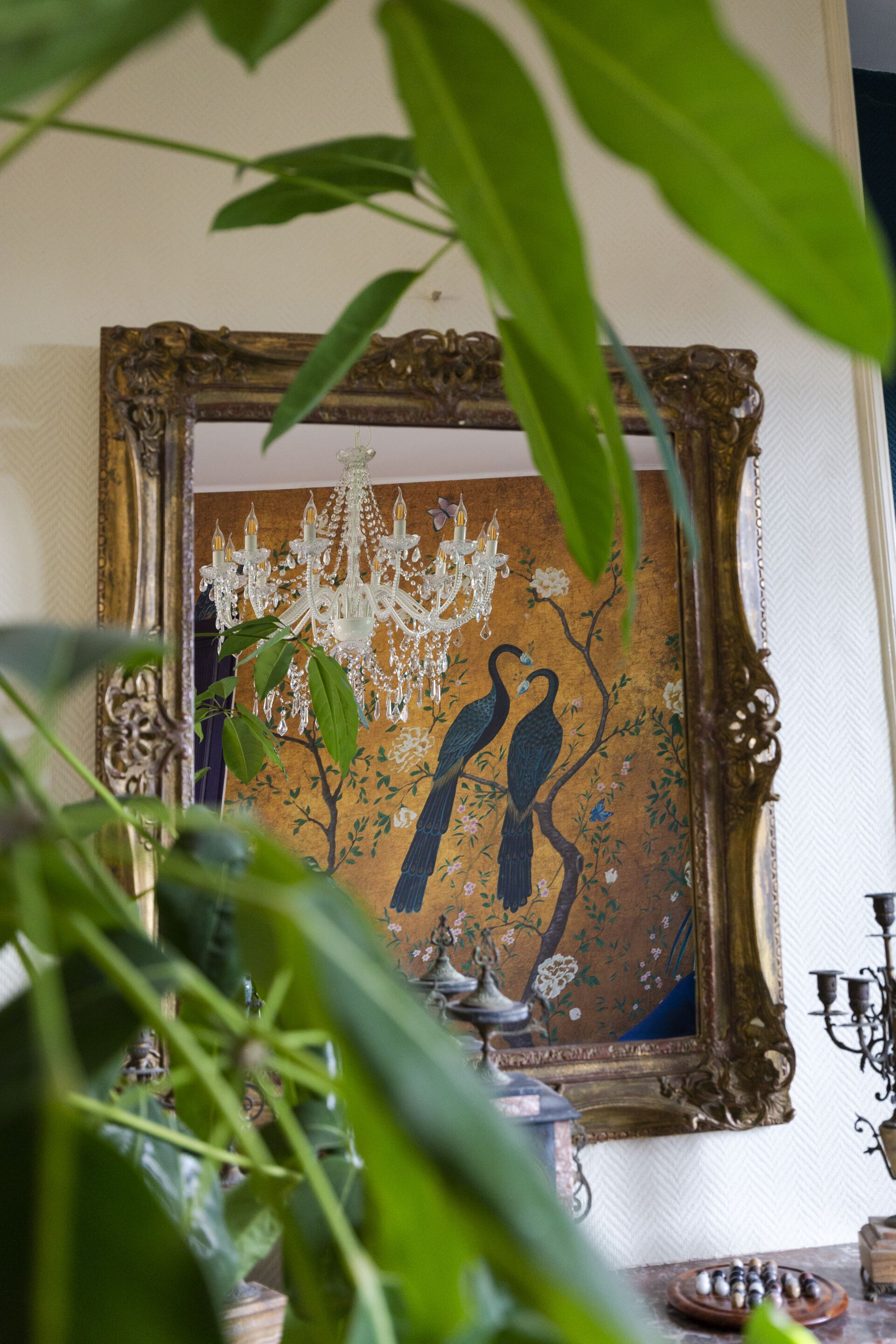 A framed painting with a chandelier and a bird on a branch.