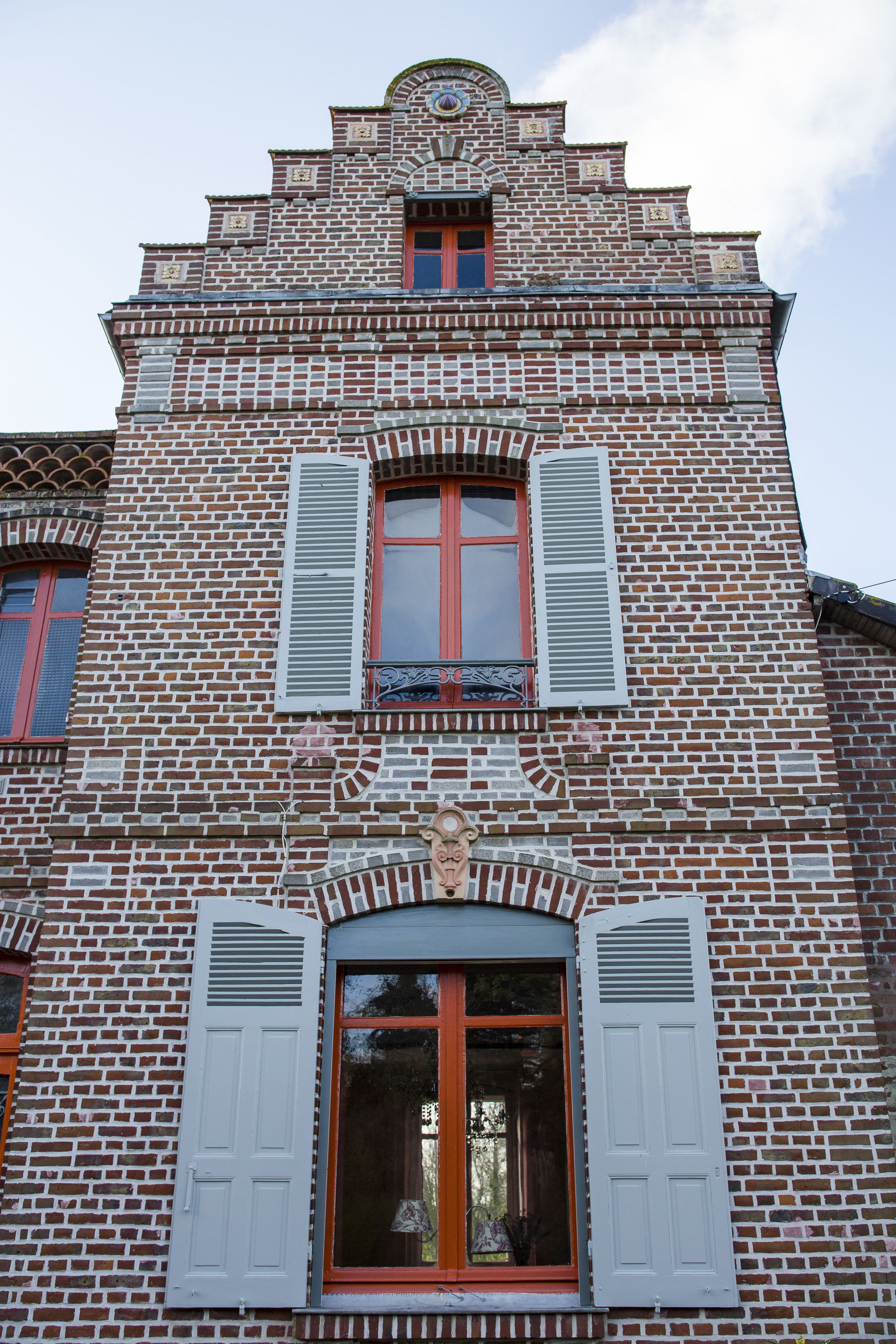 Un bâtiment à la façade en briques, doté de nombreuses fenêtres avec volets et d’éléments décoratifs.