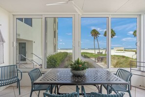 A balcony with a table and chairs, a potted plant, and a view of the beach and palm trees. - Island House Beach Resort 2S (Siesta Key)