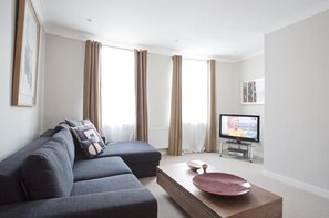 A modern living room with a grey sofa, a wooden coffee table, and a television on a stand. - Central Apartment with Wifi (London)