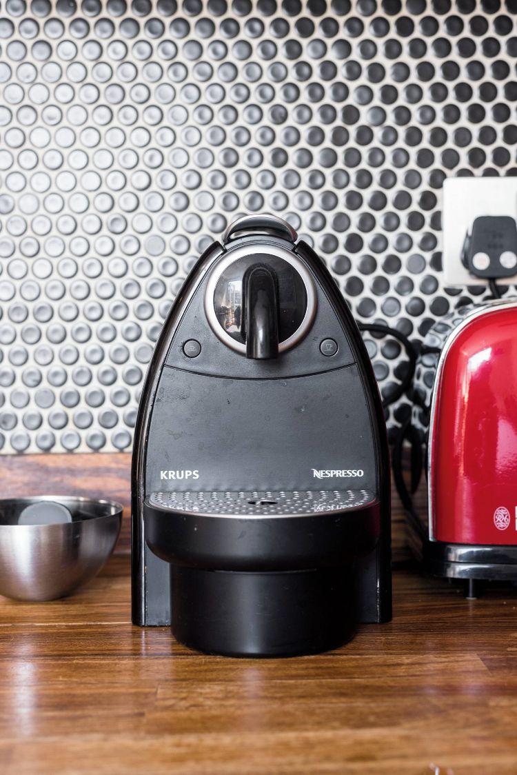 A Krups espresso machine with a Nespresso logo, a red toaster, and a metal bowl on a wooden surface.