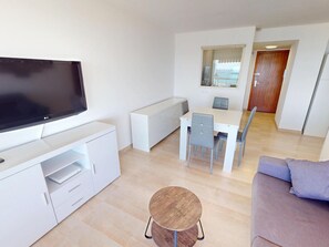 A modern living room with a flat-screen TV, a dining table with chairs, a sofa, and a small round table.