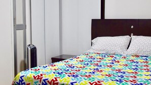 Uma cama com um edredom estampado em padrão geométrico colorido, uma cabeceira escura e um travesseiro branco.
