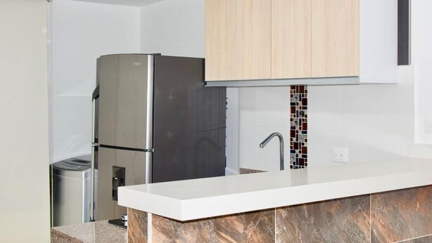 Uma cozinha moderna com geladeira embutida, pia com painel de azulejos e armários de madeira acima do balcão.
