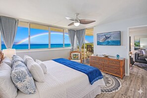 Un dormitorio con cama, cómoda, silla, televisor y vistas al océano.