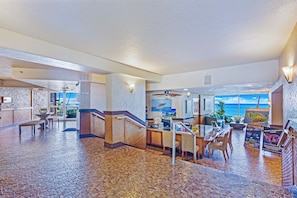 A spacious lobby with a tiled floor, a reception desk, seating area, and a view of the ocean.