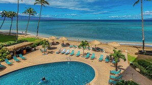 A resort pool area with lounge chairs and palm trees, overlooking a beach and ocean.