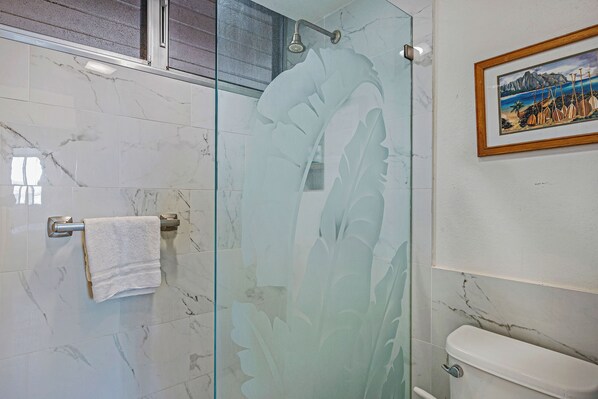 Une salle de bain avec une douche à parois de verre, des toilettes et un tableau encadré au mur.