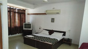 A bedroom with a bed, a television, an air conditioning unit, and a window with curtains.