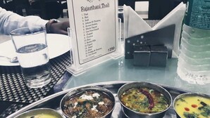 A menu board for Royal Rasoi with a list of dishes, a water bottle, and three bowls of food on a table.