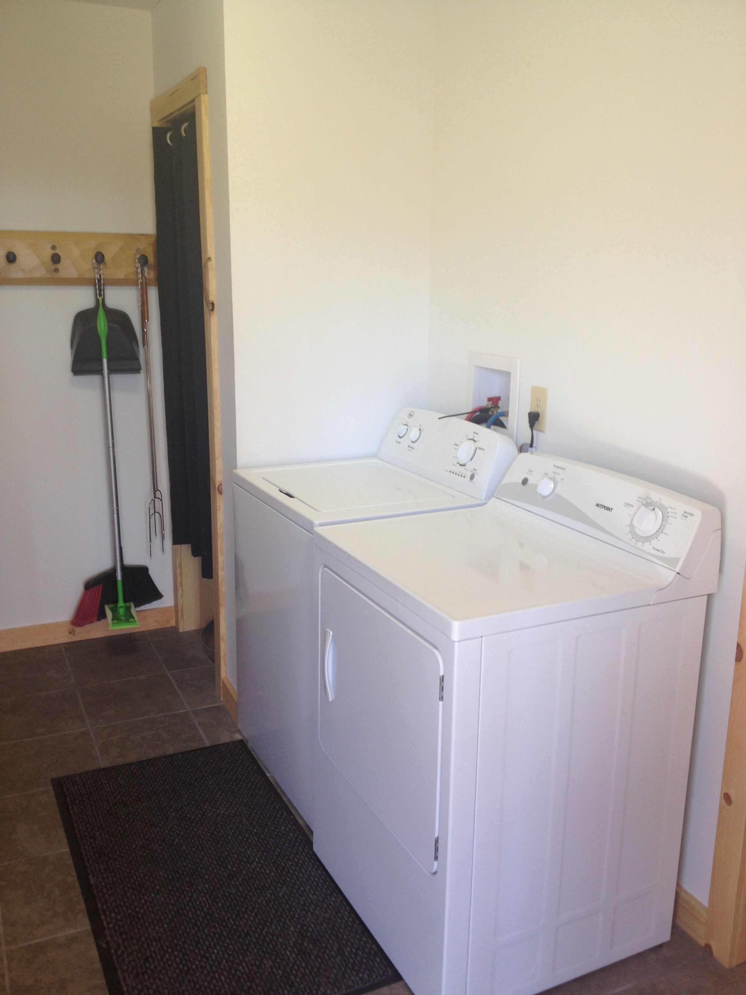 A laundry room with a front-loading washer and dryer, a broom, and a mop leaning against the wall.