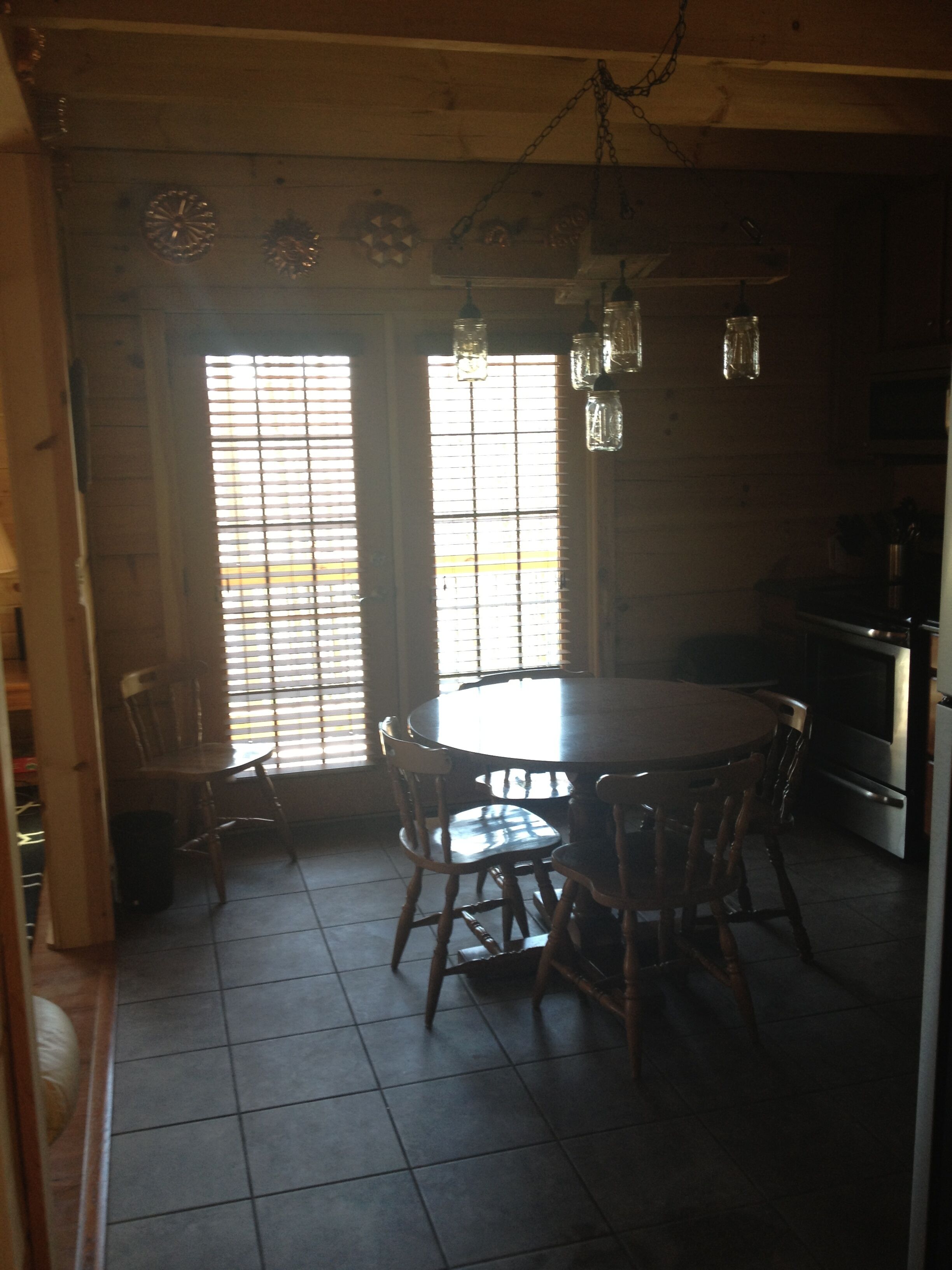 A kitchen with a round table and chairs, wooden cabinets, and a hanging light fixture.