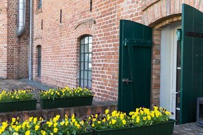 Een gebouw van baksteen met een groene deur en ramen. Voor het gebouw staan bloembakken met gele bloemen.