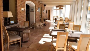 Ein Restaurant mit Backsteinwänden, Holztischen und -stühlen, und einem Hund, der durch den Raum läuft.