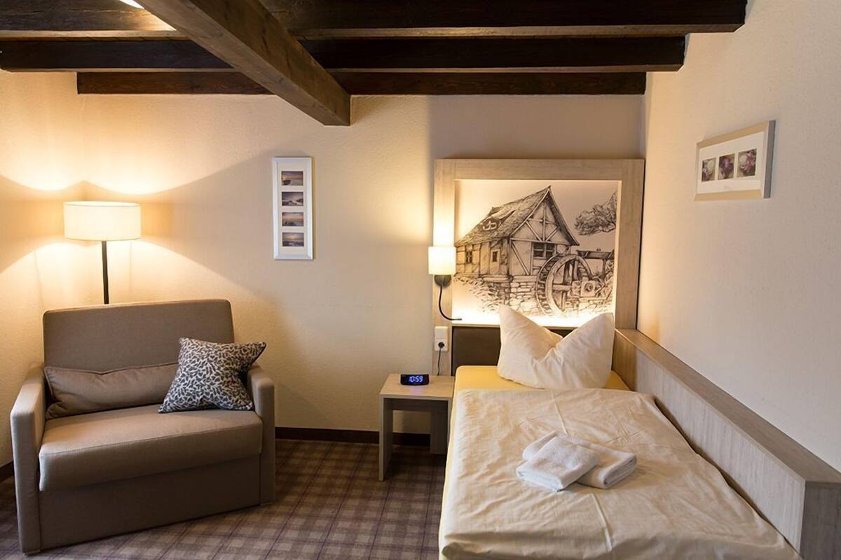 Une chambre d’hôtel avec un canapé, un lit, une table de chevet, une lampe et un tableau encadré au mur.