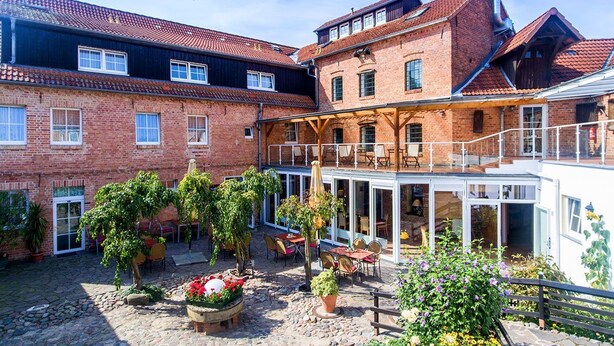 Ein Innenhof mit Außenbestuhlung, ein Backsteinhaus und eine überdachte Struktur mit Glas.