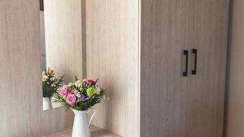 A room with a wardrobe, a mirror, and a small table with a vase of flowers.