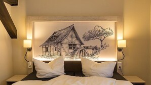 Ein Hotelzimmer mit einem Bett, zwei Nachttischlampen und einem Wandbild von einem Haus und einem Baum.