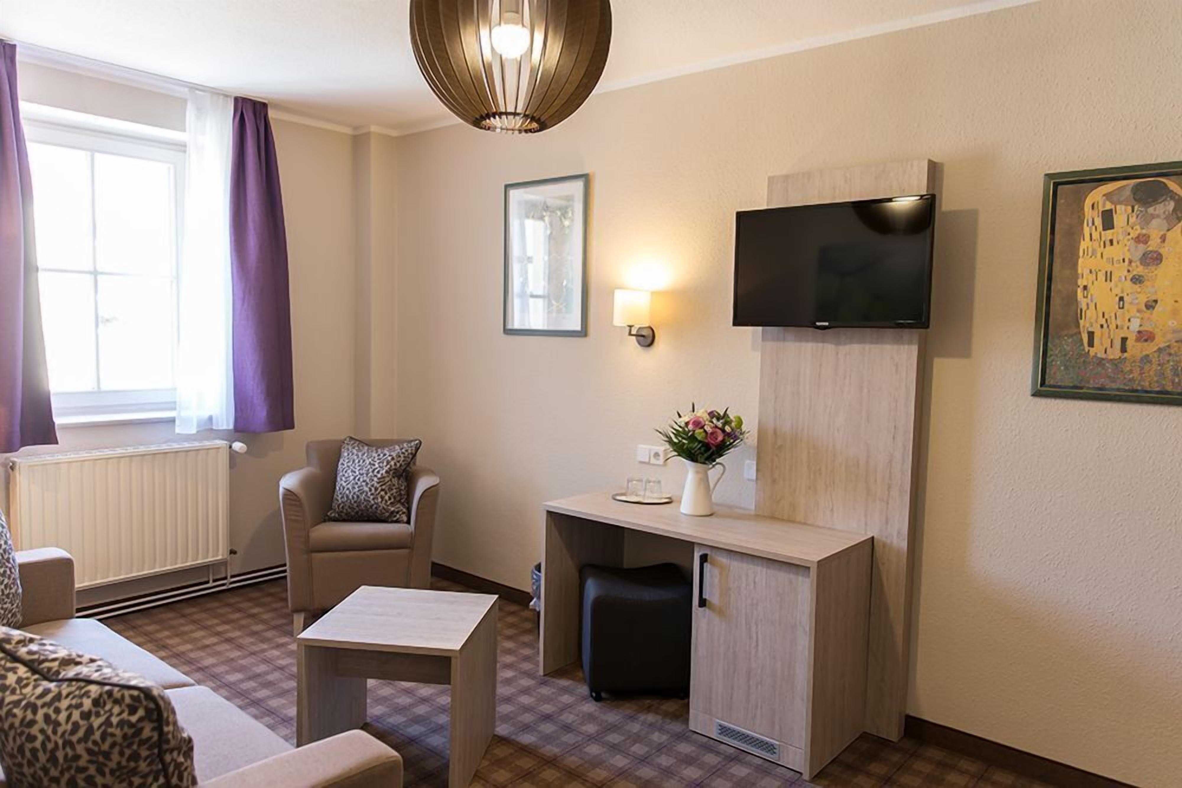 A modern hotel room with a sofa, a small table, a TV mounted on the wall, and a radiator.