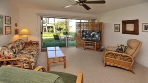 A living room with a sofa, armchair, TV, and a glass table. - Hale Kamaole #107 Ground floor condo, easy access to best beach on Maui! (Kihei)