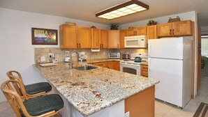 A kitchen with wooden cabinets, granite countertops, a white refrigerator, and a microwave. - Hale Kamaole #107 Ground floor condo, easy access to best beach on Maui! (Kihei)