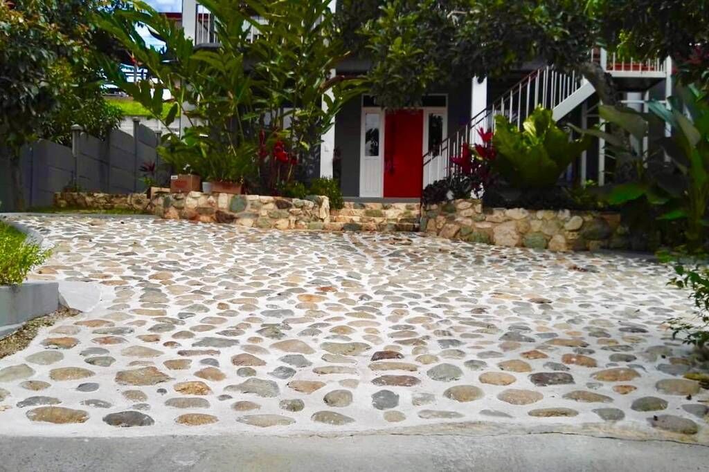 A stone-paved pathway leading to a building with a red door and a staircase.