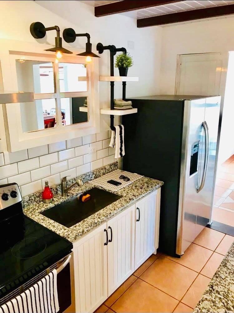 Cocina con alacenas blancas, encimera de granito, refrigerador de acero inoxidable y estufa negra.