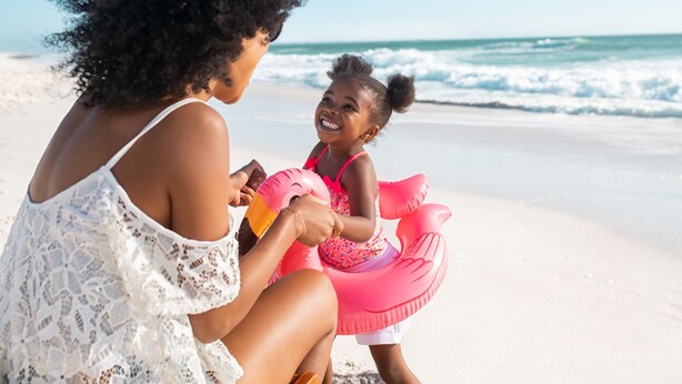 A beach scene with a person and a child on the sand, near the water.