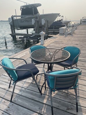 A wooden pier with a metal table and chairs, a boat docked in the background, and a clear view of the water. - Amazing SUNSETS on the BAY+ WATERFRONT- 5 min walk to Beach+ Boardwalk (Ocean City)