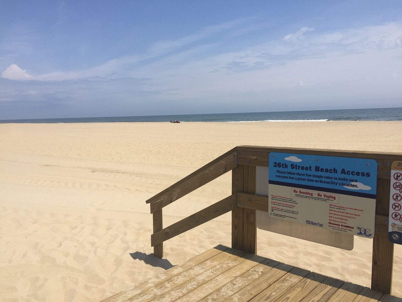 Een houten looppad dat naar een strand leidt, met een bord waarop de strandregels staan.
