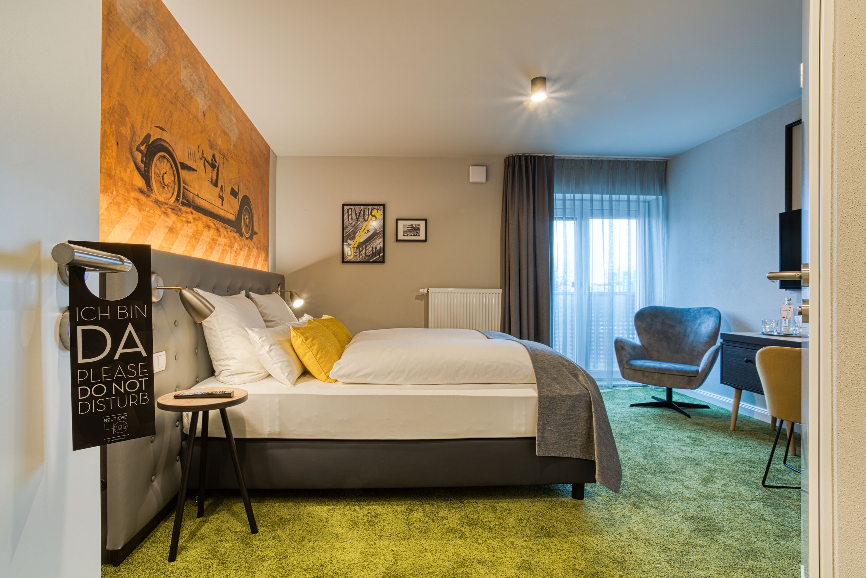 Hotelkamer met een groot bed, een bureau, een stoel, een radiator, een raam met gordijnen en een muur met een groot schilderij en een bord.