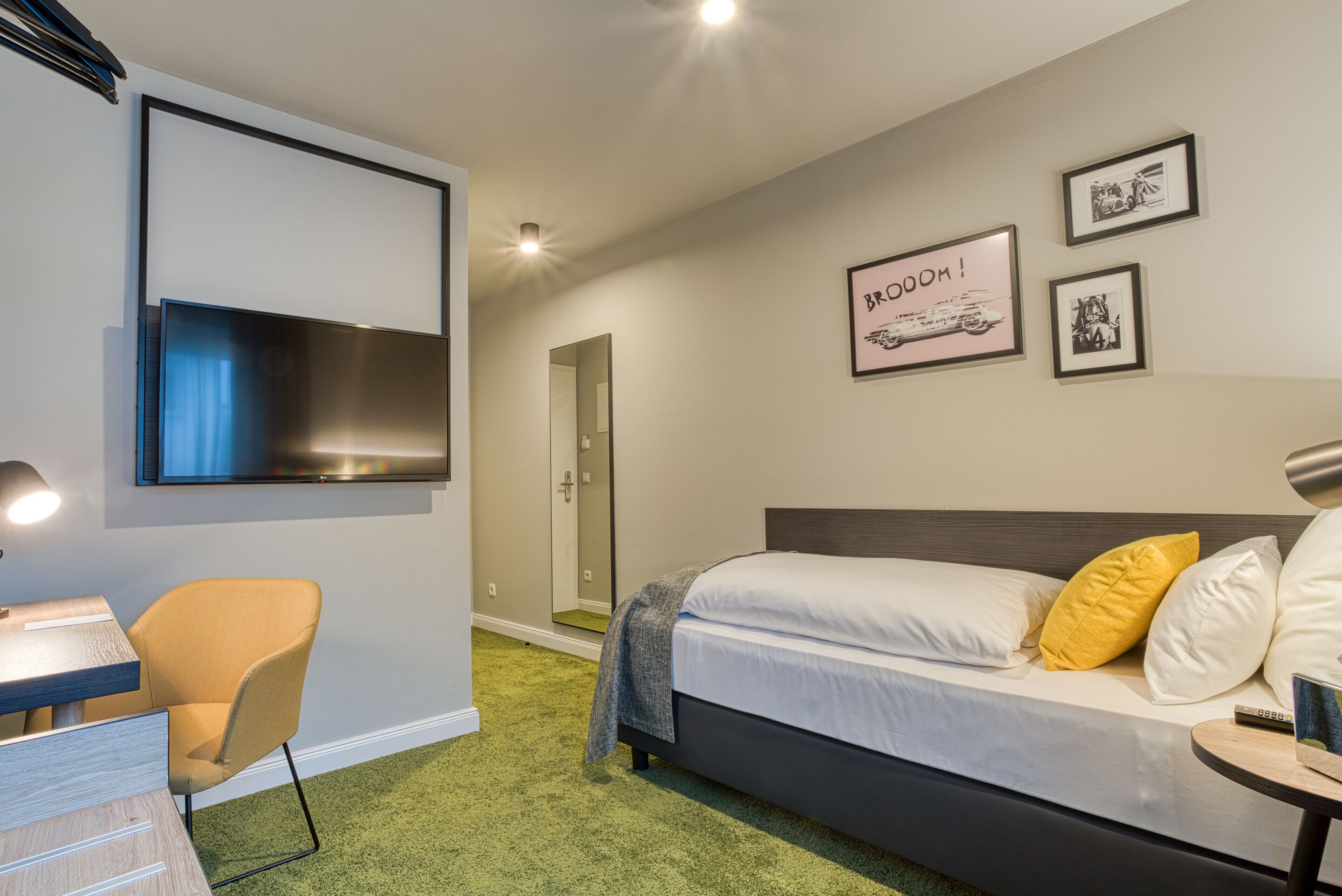 Een moderne hotelkamer met een bed, een bureau, een stoel en een televisie aan de muur.