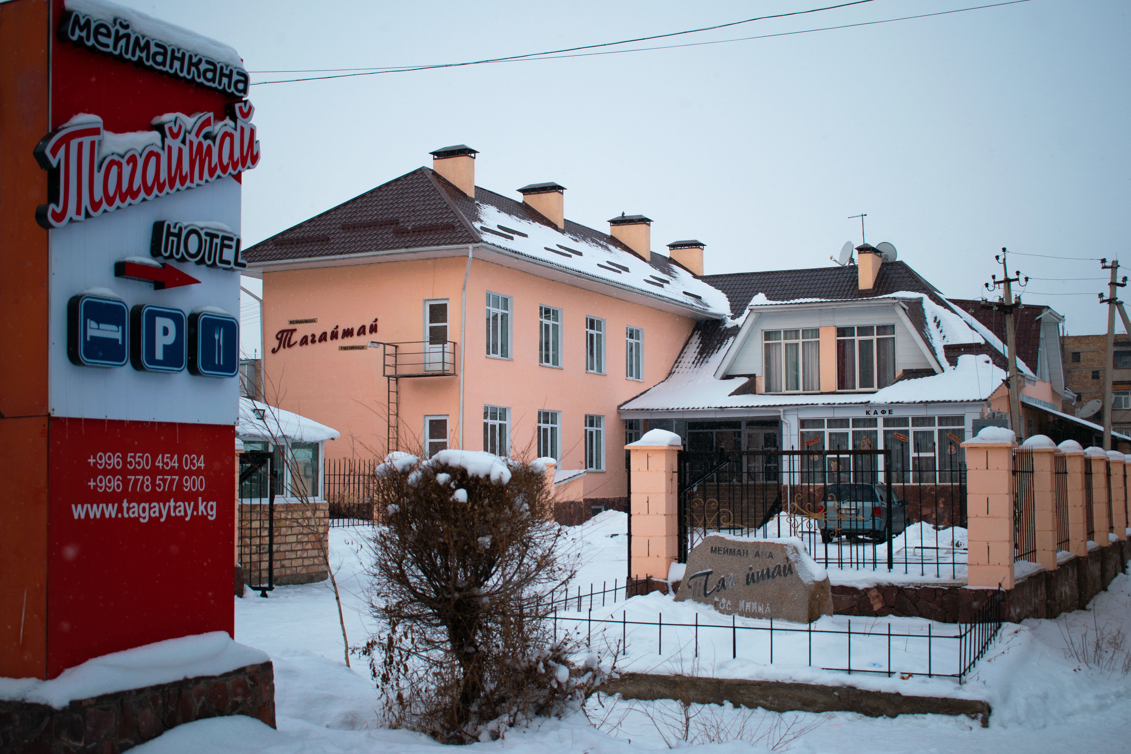 Letrero de hotel con datos de contacto y un edificio cubierto de nieve con entrada porticada.