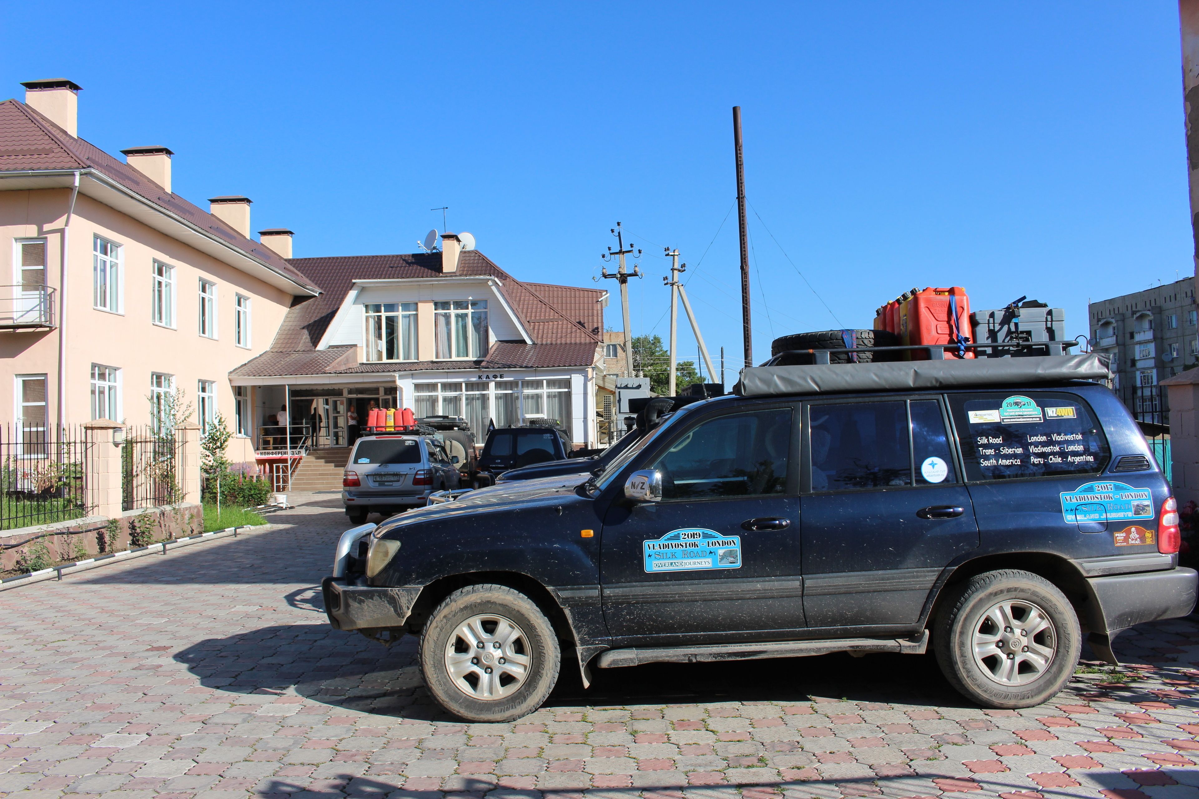 A vehicle parked on a cobblestone street in a residential area with houses and a clear blue sky.