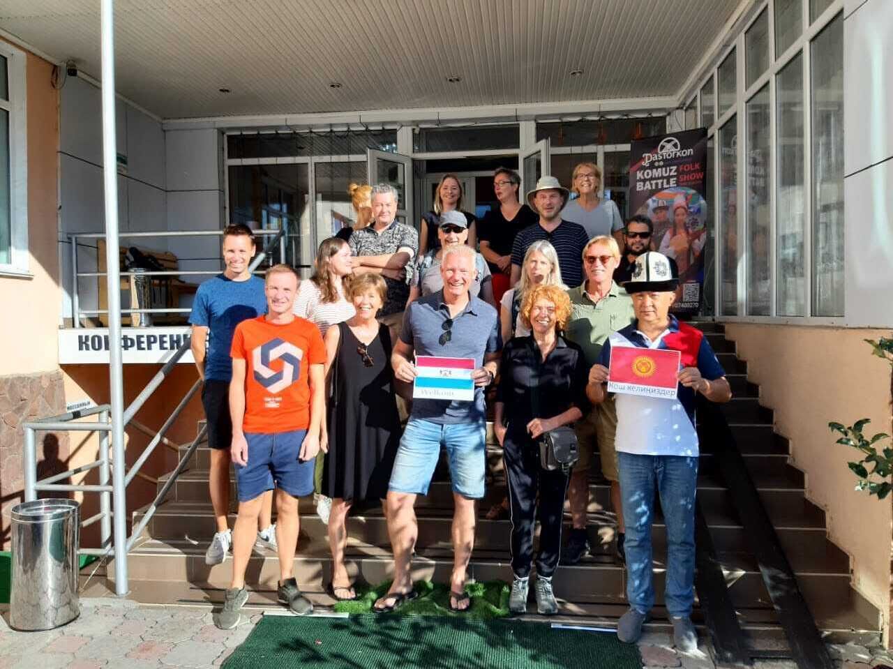 Un groupe de personnes se tient sur un escalier à l’extérieur d’un bâtiment, devant une enseigne sur laquelle on peut lire : « KOMUZ FOLK BATTLE SHOW ».