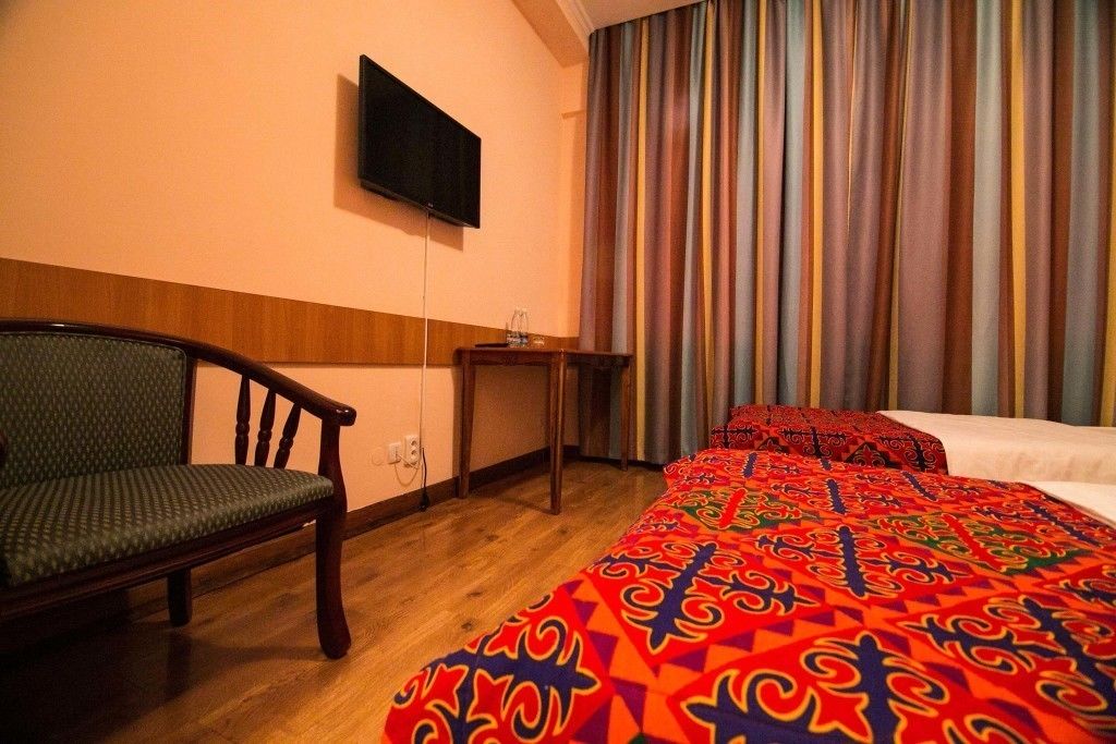 Une chambre d’hôtel avec un lit, une chaise, une petite table, un téléviseur fixé au mur et des rideaux.