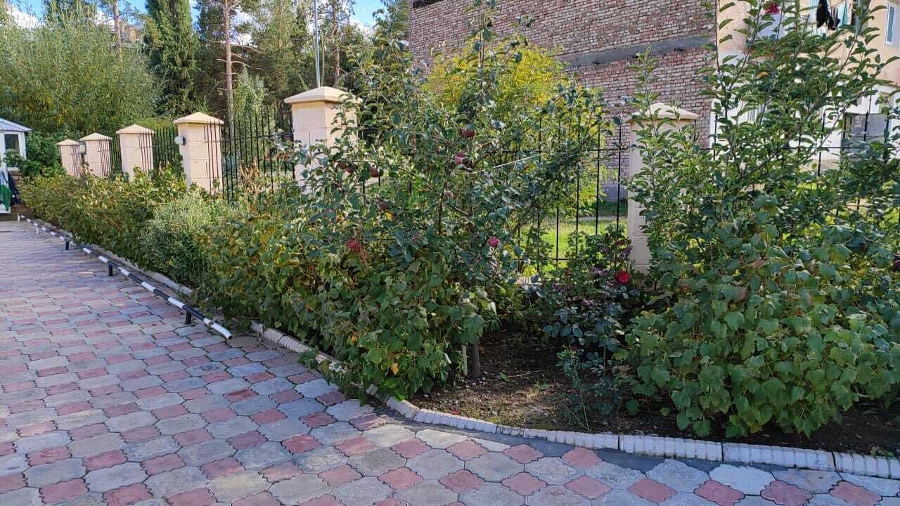 A paved pathway lined with lush greenery and a brick building in the background.