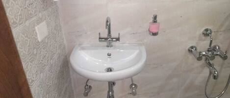 A bathroom with a white sink, a pink soap dispenser, and a shower with a chrome faucet.