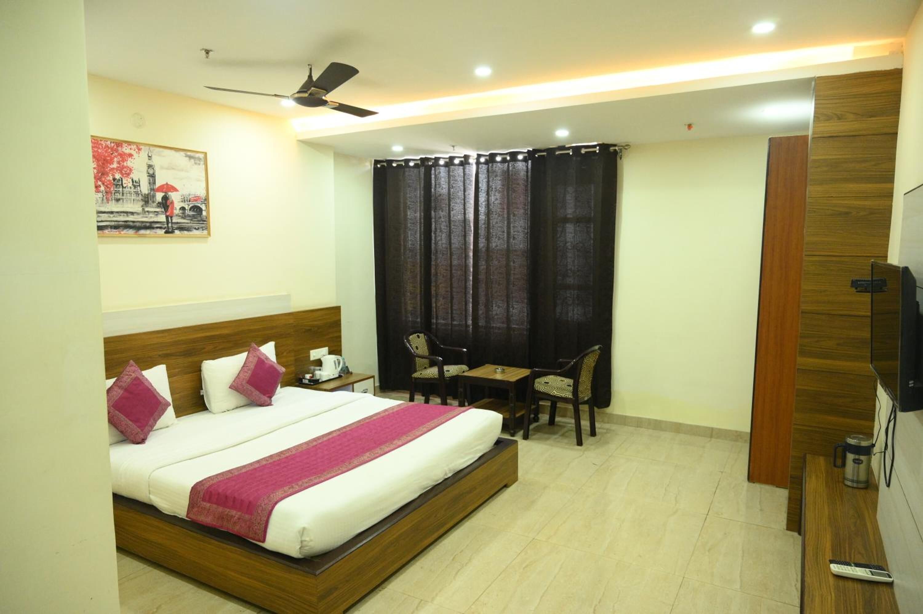 Habitación de hotel con cama, escritorio, dos sillas, televisor y ventilador de techo.