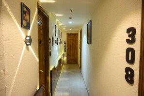 Un pasillo de hotel con una puerta de madera al final, el número 308 en la pared, y un letrero de tienda a la izquierda.