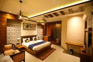 A modern hotel room with a large bed, a desk, a chair, a small table, a TV, and a ceiling fan. - Hotel Grand Kailash (Lansdowne)